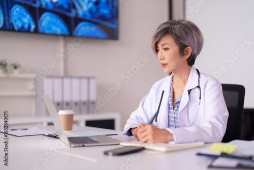 Wallpaper Mural Asian adult female physician diligently reviews medical scans patient data on laptop computer in a professional healthcare clinic office Torontodigital.ca