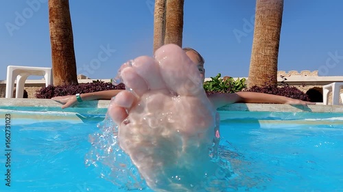 Carefree young girl experiencing joyful summer moments, splashing and playing in bright blue resort swimming pool surrounded by palm trees, radiating pure childhood happiness
