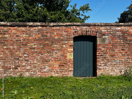 Wooden painted garden gate in a brick wall with green grass in foreground