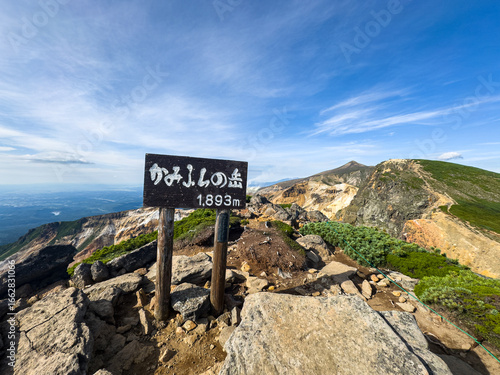 Tokachi-dake and Kamihorokamettoku ridgeline viewed from the summit of Mount Kamifurano in the Daisetsuzan Range, Hokkaido, Japan, with rugged volcanic terrain and clear summer sky.