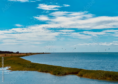 Coastal landscape of Kalvebod Fælled in Naturpark Amager, Denmark with blue sea, green wetlands, and kite surfers in the distance