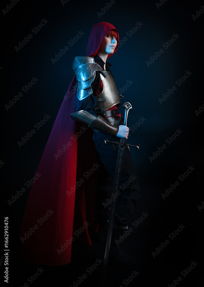 Naklejka premium Fantasy warrior woman with red hair in historical medieval armour costume and red fairytale cloak, cinematic studio portrait of strong heroine knight, dramatic standing profile silhouette figure.