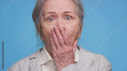 Shocked senior woman reacting to bad news on blue background