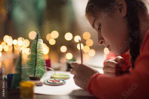 child paints handmade Christmas tree decoration made from salt dough. girl makes crafts for the new year in school