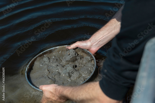 Bild auf Leinwand Hands holding container with wet soil sediment sample showing muddy texture and