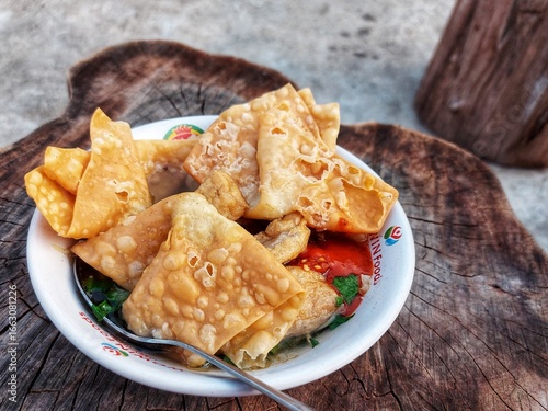 Indonesian meatballs served with noodles, tofu, and fried wontons (pangsit) on a wooden table.street food.
