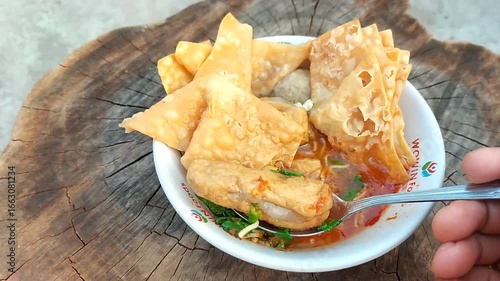 Indonesian meatballs served with noodles, tofu, and fried wontons (pangsit) on a wooden table.street food.