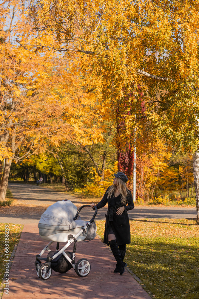 Obraz premium Beautiful young girl in black clothes and a black cap with a baby carriage in her hands in an autumn park. autumn season. autumn mood. autumn. mother. motherhood mother's day