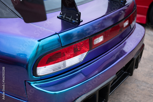 Close-up of the rear taillights and wing mounts on with an iridescent blue and purple vinyl wrap, showcasing its custom JDM tuning