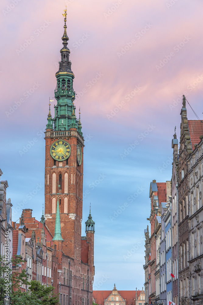 Fototapeta premium Gdansk, a city on the Baltic coast of northern Poland, Europe. Majestic tower clock dominates historical cityscape against pink-tinged sky, showcasing architectural grandeur and timeless elegance.