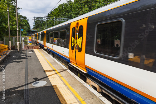 London Overground train at suburban station platform, orange livery, London, UK