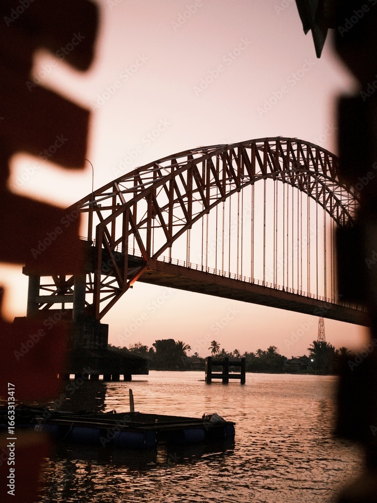 Naklejka premium A bridge standing over a river and the morning atmosphere with the sunlight starting brighten the sky