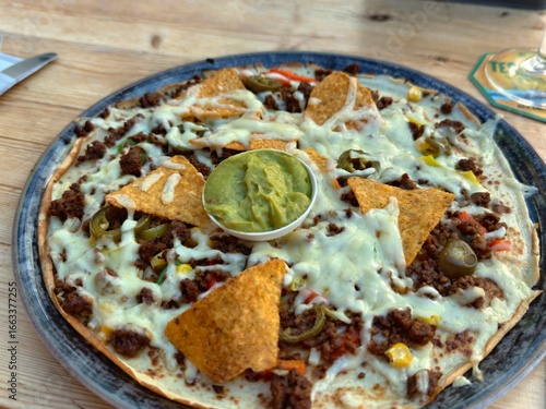 Delicious nachos pizza with melted cheese guacamole and tortilla chips ready to eat