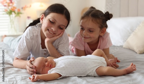 Big sisters admiring newborn baby on bed at home