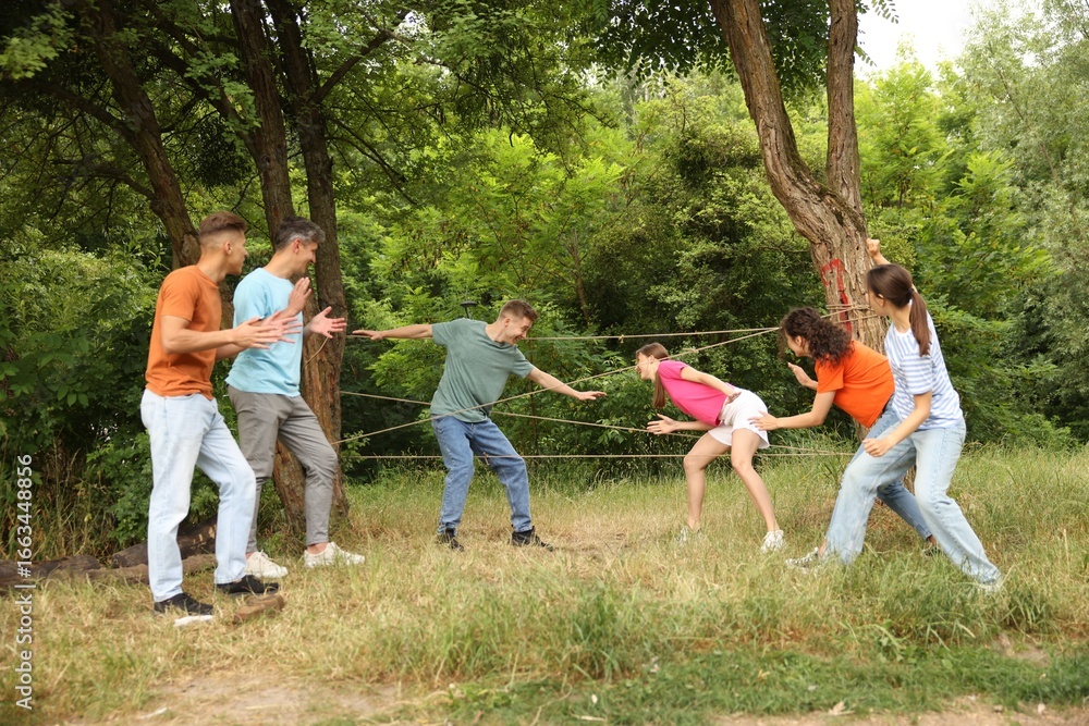 Fototapeta premium Team building. Group of happy people playing spider web game outdoors