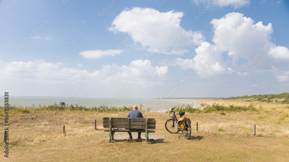 Obraz premium cycliste assis sur un banc face à la mer. senior, homme âgé profitant du paysage face à l'océan. Scène calme et tranquille en été
