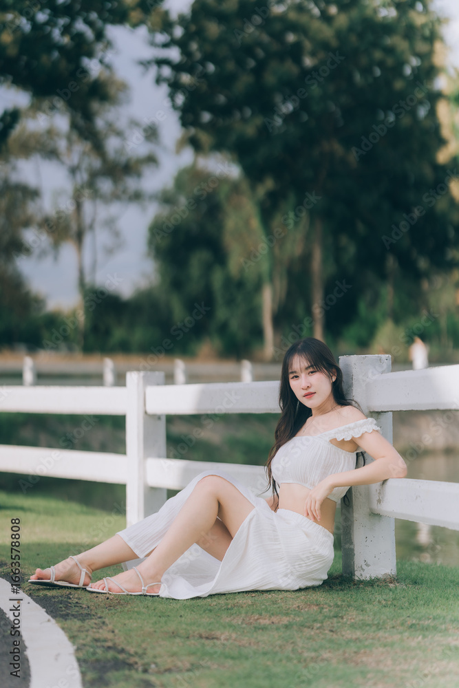 Naklejka premium Serene Portrait in the Park: A young woman finds a moment of peace, leaning against a fence in a park, the sunlight gently caressing her.