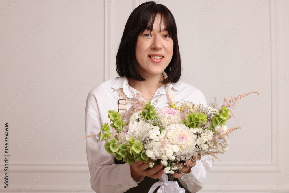 Florist with beautiful bouquet of flowers near white wall indoors Florist with beautiful bouquet of flowers near white wall indoors