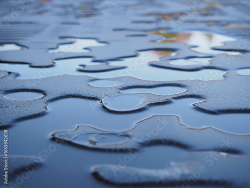Fototapeta Abstract close up of puddles on a textured surface reflecting the sky and surrou