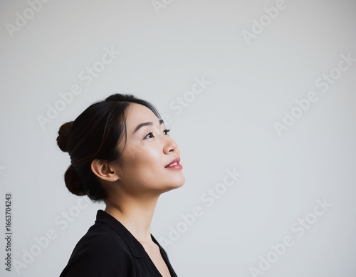 Profile of asian woman with hair in bun looking up against a plain light gray background