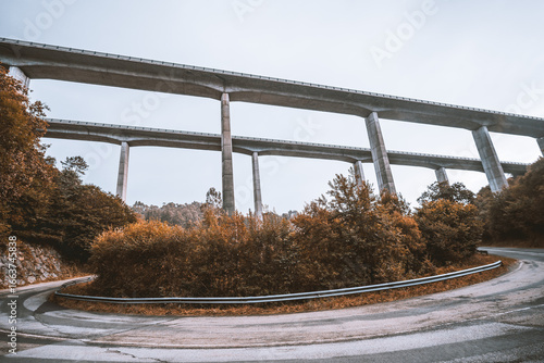 Wide-angle view of two elevated highways running one behind another above autumn trees and a winding mountain road, showcasing impressive modern transport infrastructure