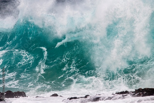 Blue wave crashing on coastal  rocks