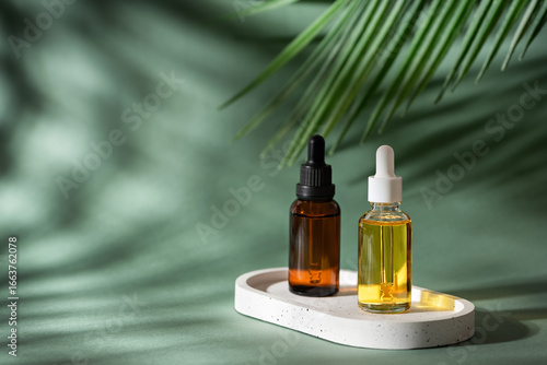 Various dropper bottles with cosmetic skin care serum on green background with palm leaf, anti-aging cosmetic products, essential oils