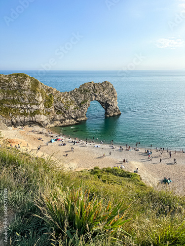 Durdle Door limestone arch on the Jurassic Coast in Dorset. Natural landmark.Summer holidays England. Crowded beach, people are spending summer weekend in English seaside. Pure clean clear water.