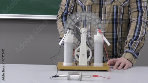 Physics demonstration of electrostatics experiment showing the transfer of electric charge between objects. Teacher explains principles of static electricity to students during a classroom lesson.