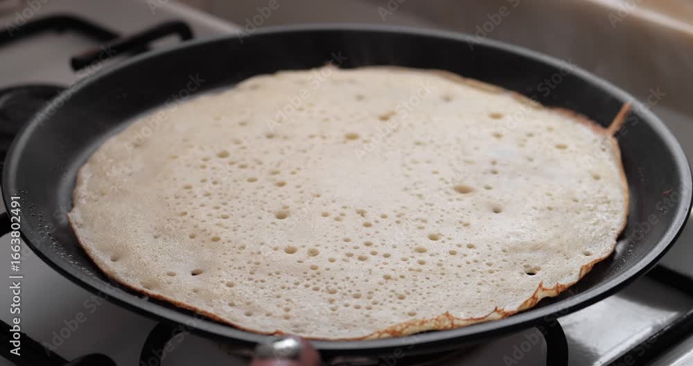 custom made wallpaper toronto digitalA thin pancake cooking in a black frying pan on a gas stove. Bubbles form on the surface as it cooks evenly.