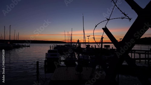 Boats and masts in silhouette at sunset in the marina of Berlin’s Lake Wannsee, with calm water and warm evening sky.