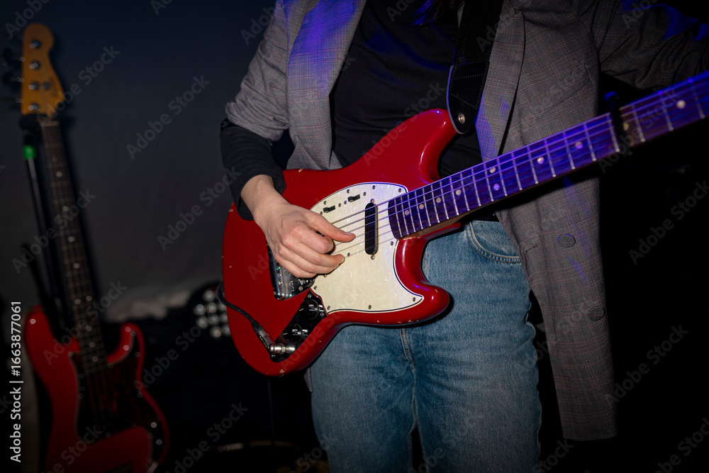 Obraz premium Musician playing red electric guitar in concert setting with blue lighting