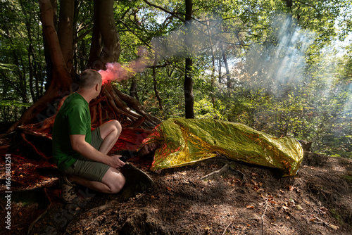 Obraz na plátně Person using red signal flare at makeshift forest shelter during survival traini