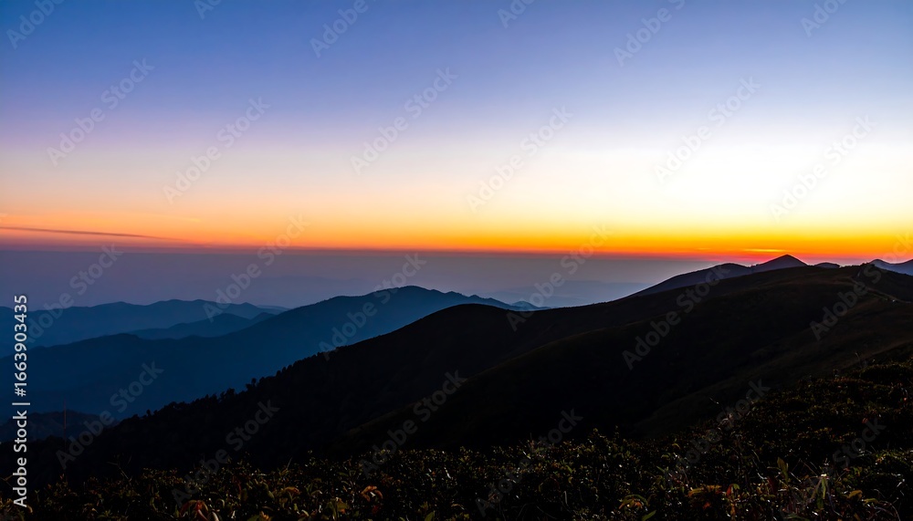Fototapeta premium A breathtaking panorama of mountain ranges at sunrise, showcasing a vibrant color gradient across the sky and rugged terrain.
