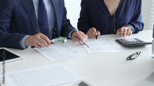 Chartered accountants analyzing financial reports with a magnifying glass and calculator for precise compliance verification. Audit and taxes in business