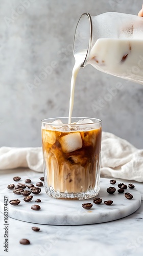 Pouring creamy milk into iced coffee creates a refreshing swirl, perfect for a summer cafe vibe