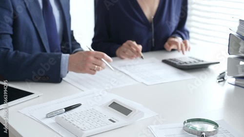 Close up of calculator and magnifying glass over financial documents opposite financial team analyzing data, reviewing reports, collaborating at modern office workspace. Audit and taxes in business