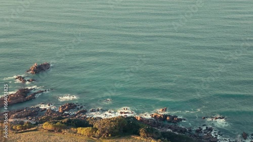 Wide shot looking down onto waves gently washing onto a rocky shoreline.