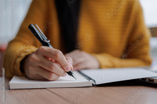 Woman writing notes on notebook with pen at wooden table