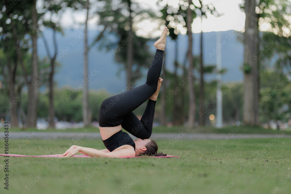 Fototapeta premium Asian woman practicing yoga peacefully in the park after work, finding relaxation and balance at sunset.