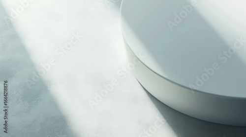 White cylindrical platform with sunlight shadows on light gray surface.