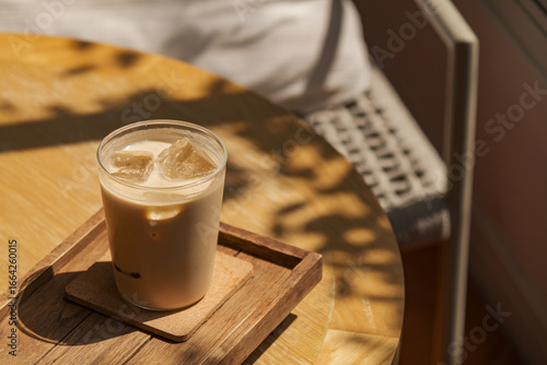 a glass of iced milk coffee on wooden table in sun light and shade