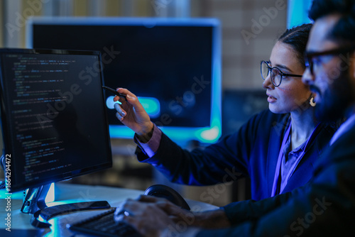 Obraz w ramie diverse AI developers collaborate in a late-night coding session. A senior engineer mentors his colleague as they program a complex machine learning algorithm together.