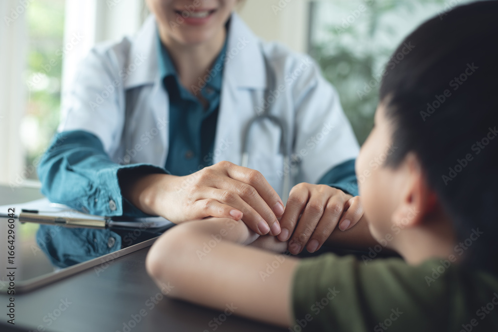 Obraz premium Female pediatrist doctor reassuring her young boy patient at medical clinic. Doctor holding her patient hand, closeup. healthcare and medicine concept.