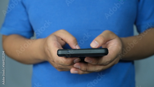 Close-up of a person in a blue shirt holding a smartphone with both hands, focused on screen interaction and digital communication.
