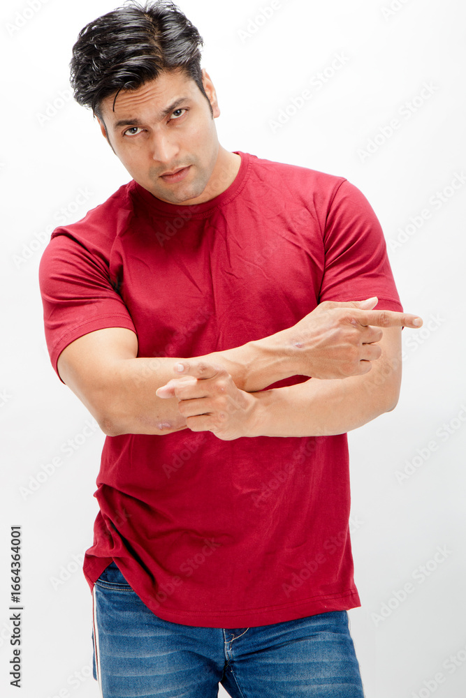 Obraz premium Young man wearing a red t-shirt, denim jeans, and sneakers posing casually in a studio against a plain white background. Ideal for themes of fashion, confidence, and modern lifestyle.