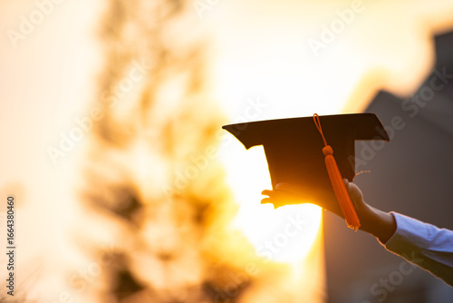 Fotografie Graduation cap held by hand during sunset, symbolizing achievement and celebrati