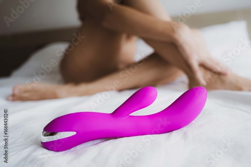 Sexy nude young woman with black mask and dildo posing in the bedroom