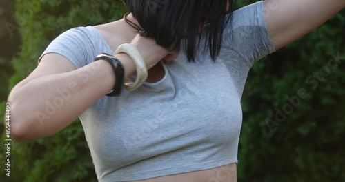 Woman with short black hair taking off her shirt on hot summer day and seeing that her armpits are wet. Concept of hyperhidrosis, sweat odor and excessive sweating.