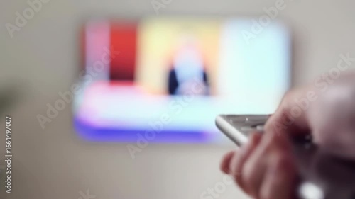 Close-up of a hand holding a remote control in front of a TV showing a news program